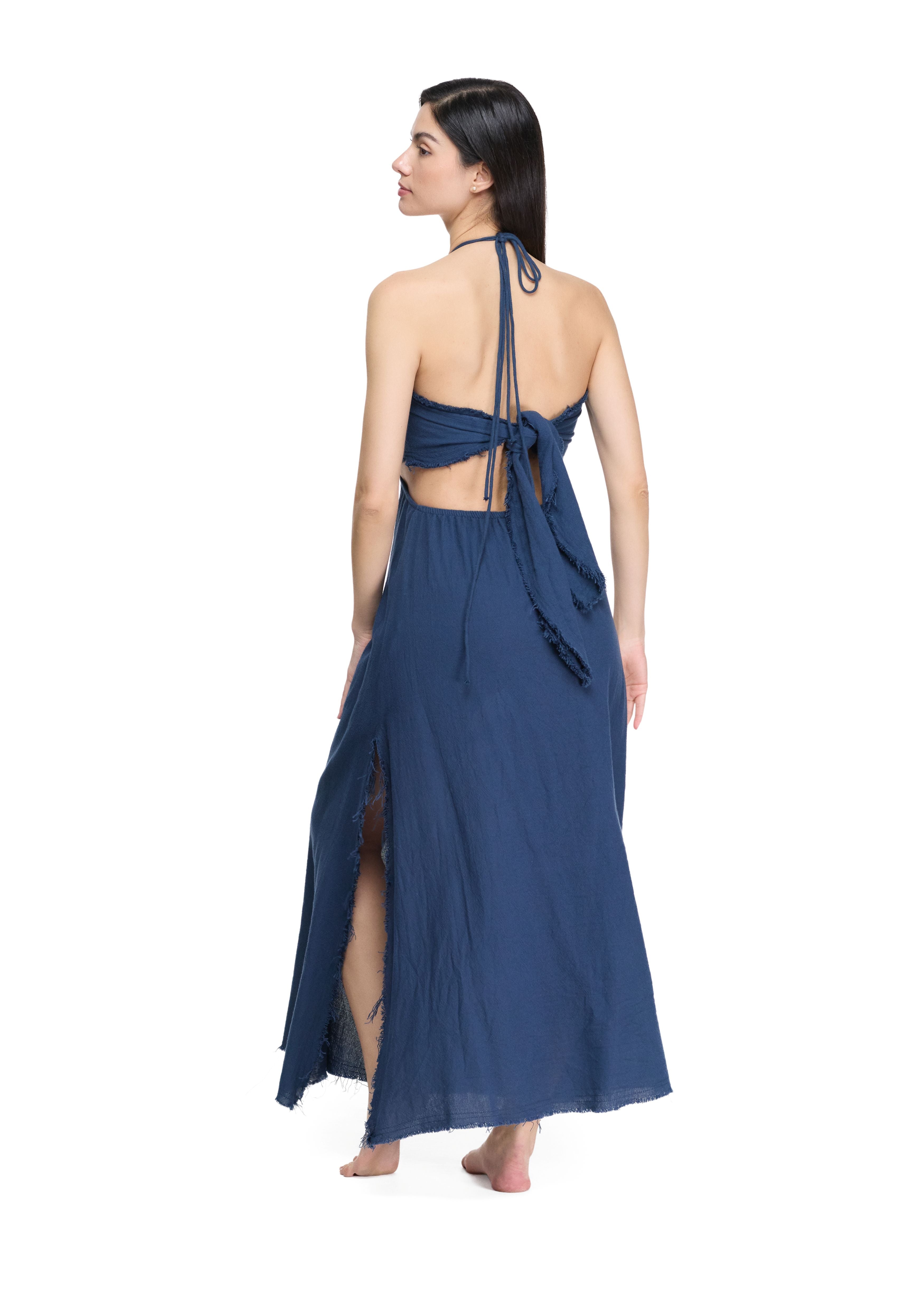 Back view of flowy navy maxi dress, open back with waist tie knot, halter cords, raw fringe hem, side slit skirt panel.