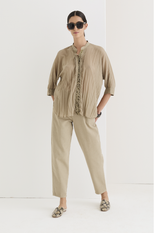 Taupe pleated linen-blend shirt with lace-up neckline, worn open over matching straight-leg trousers, styled with snake-print mules and studded sunglasses.
