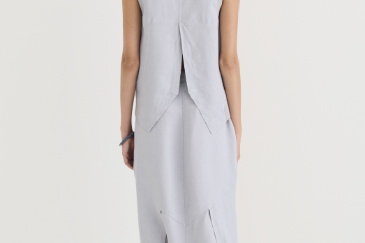 Back view of the misty gray asymmetric skirt paired with a matching sleeveless vest, both in soft garment-dyed fabric. The vest splits into a soft V at the back hem, while the
