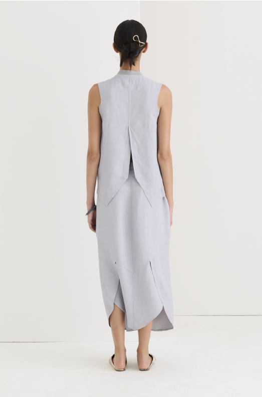 Back view of the misty gray asymmetric skirt paired with a matching sleeveless vest, both in soft garment-dyed fabric. The vest splits into a soft V at the back hem, while the