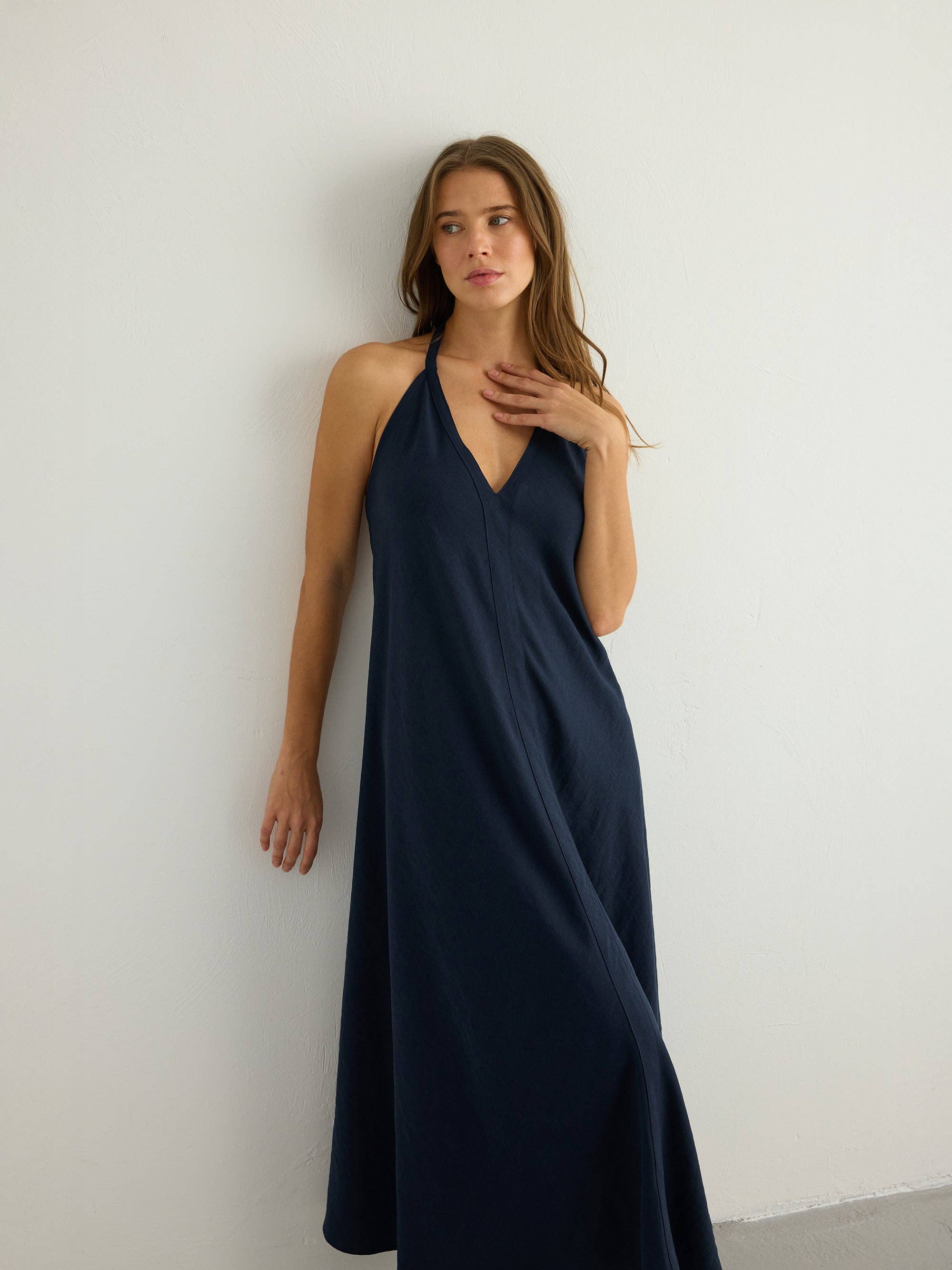 Deep navy halter maxi dress with V-neckline and subtle center front seam, A-line silhouette skimming to the floor, slub-textured natural fabric with soft matte finish.