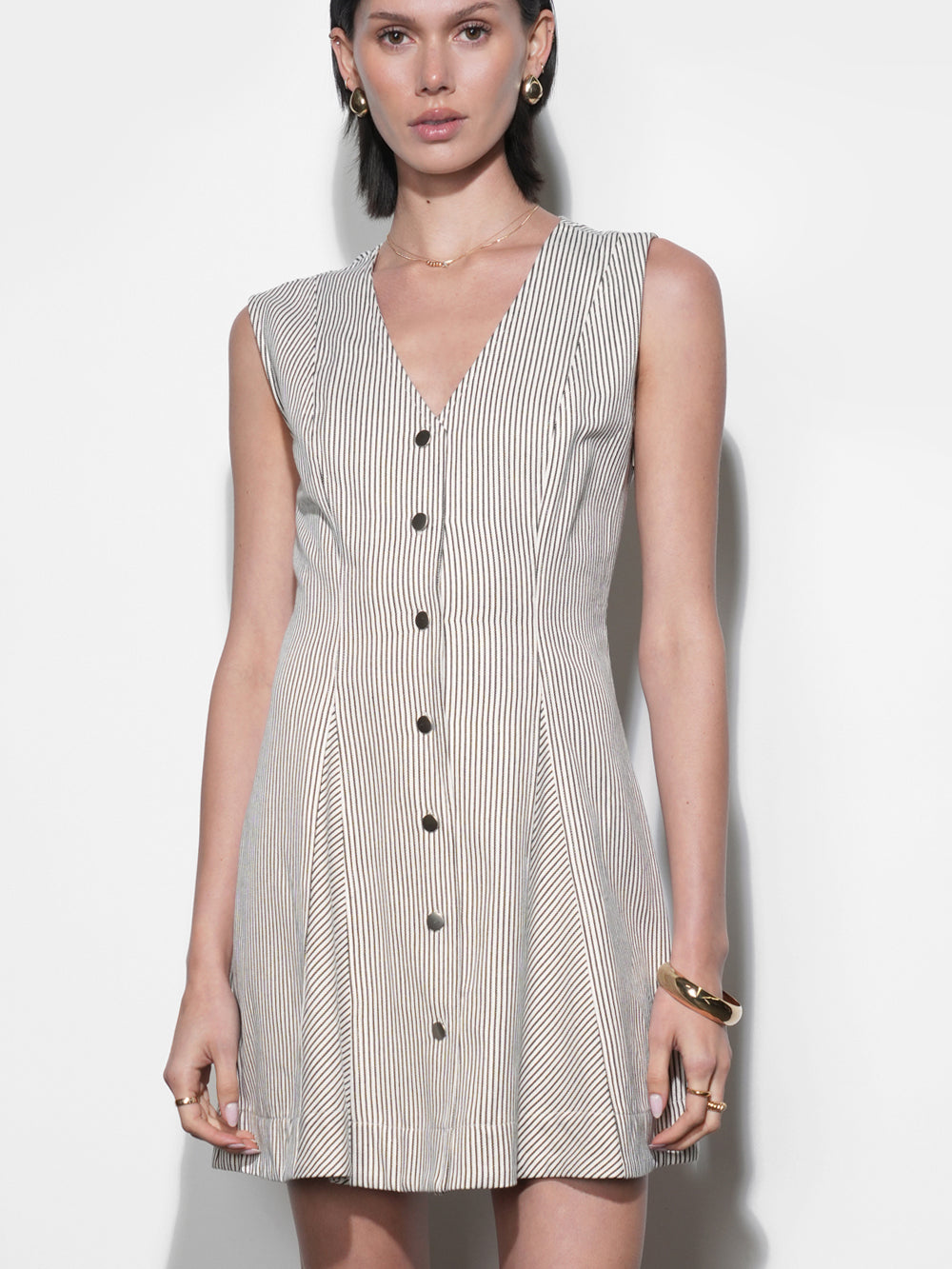 Fitted cream and black ticking stripe mini dress, deep V-neck, matte brass snap buttons, flared paneled skirt, sleeveless, styled with gold jewelry.