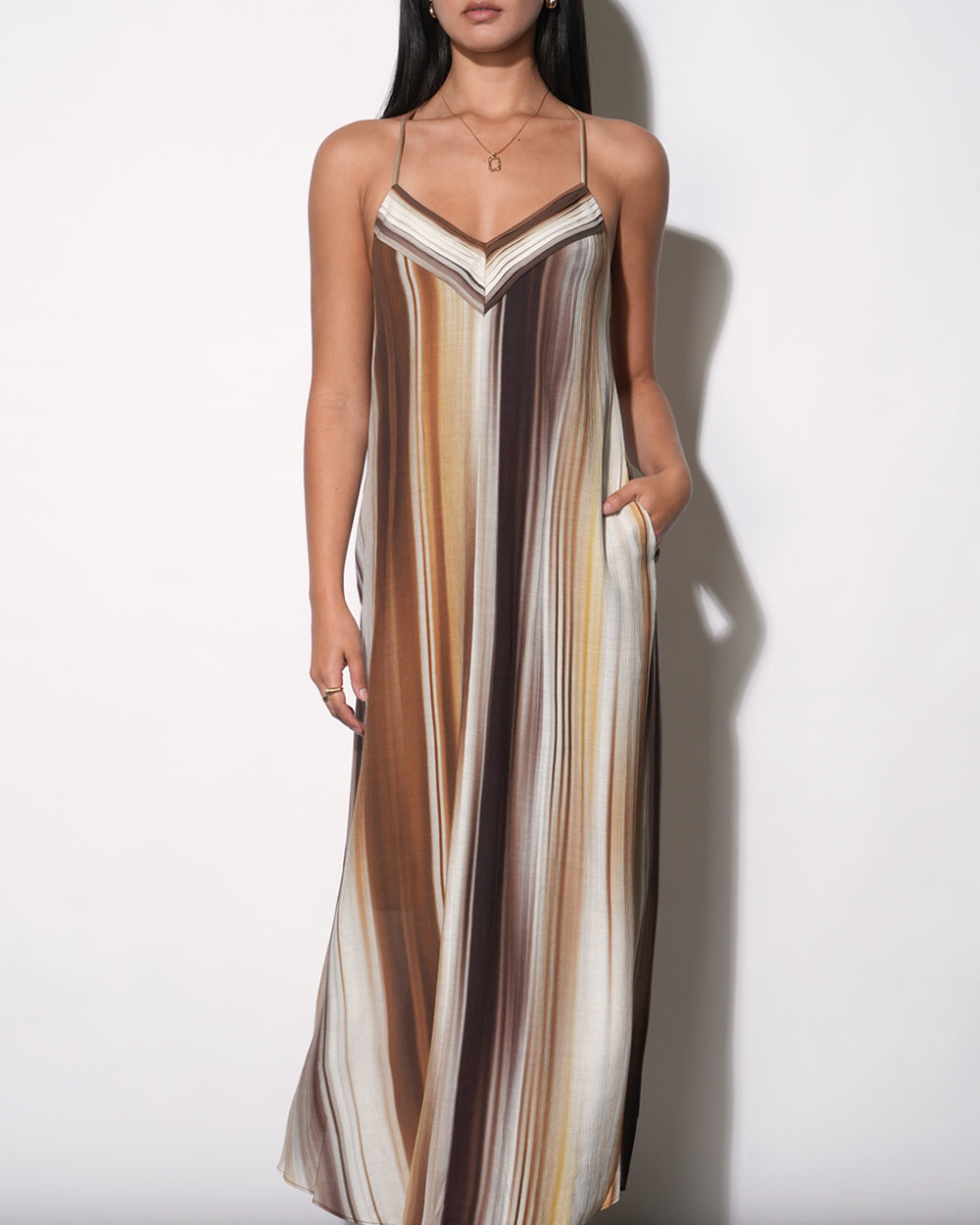 Fluid maxi dress with vertical watercolor stripe print in warm earth tones, V-neckline with contrast binding, thin spaghetti straps, relaxed A-line silhouette to floor, side pocket visible, paired