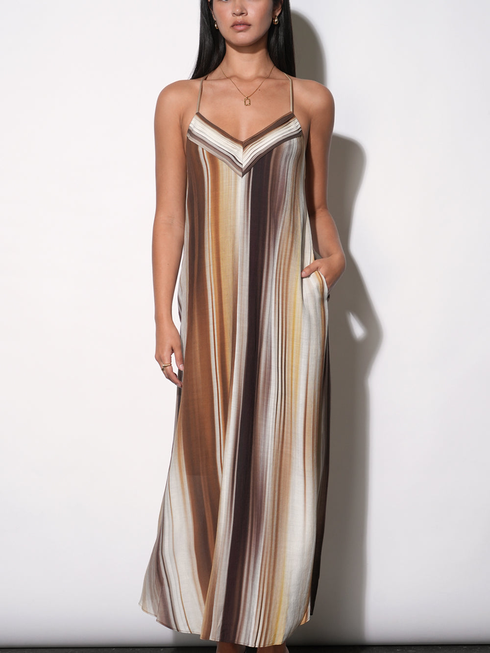 Fluid maxi dress with vertical watercolor stripe print in warm earth tones, V-neckline with contrast binding, thin spaghetti straps, relaxed A-line silhouette to floor, side pocket visible, paired