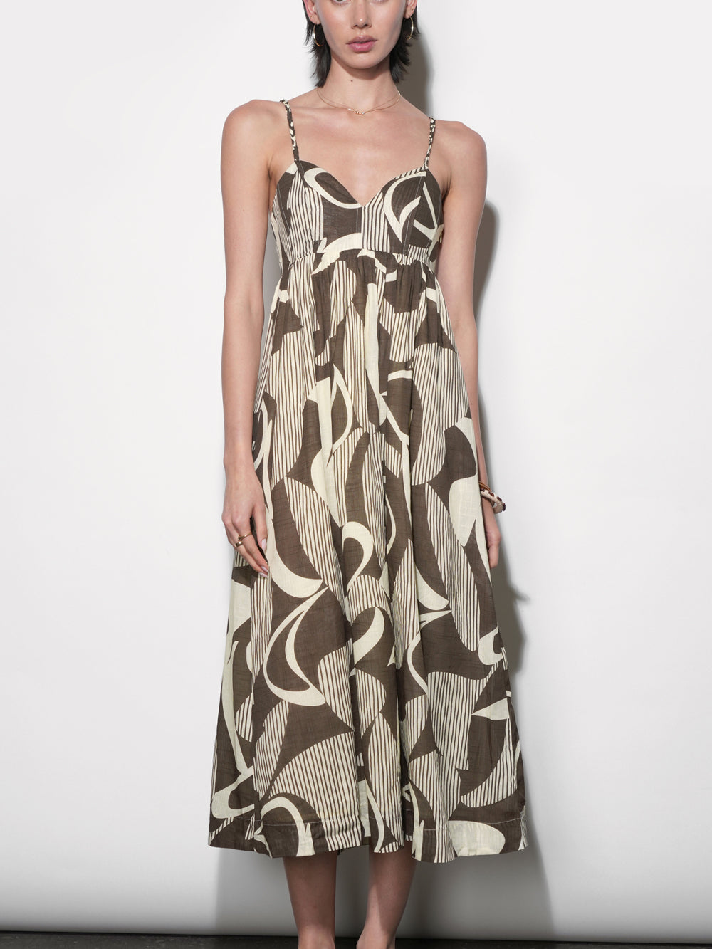 Midi dress in brown and cream abstract print with fine stripe texture, sweetheart neckline, thin woven straps, empire waist, full gathered skirt. Styled with tan strappy sandals