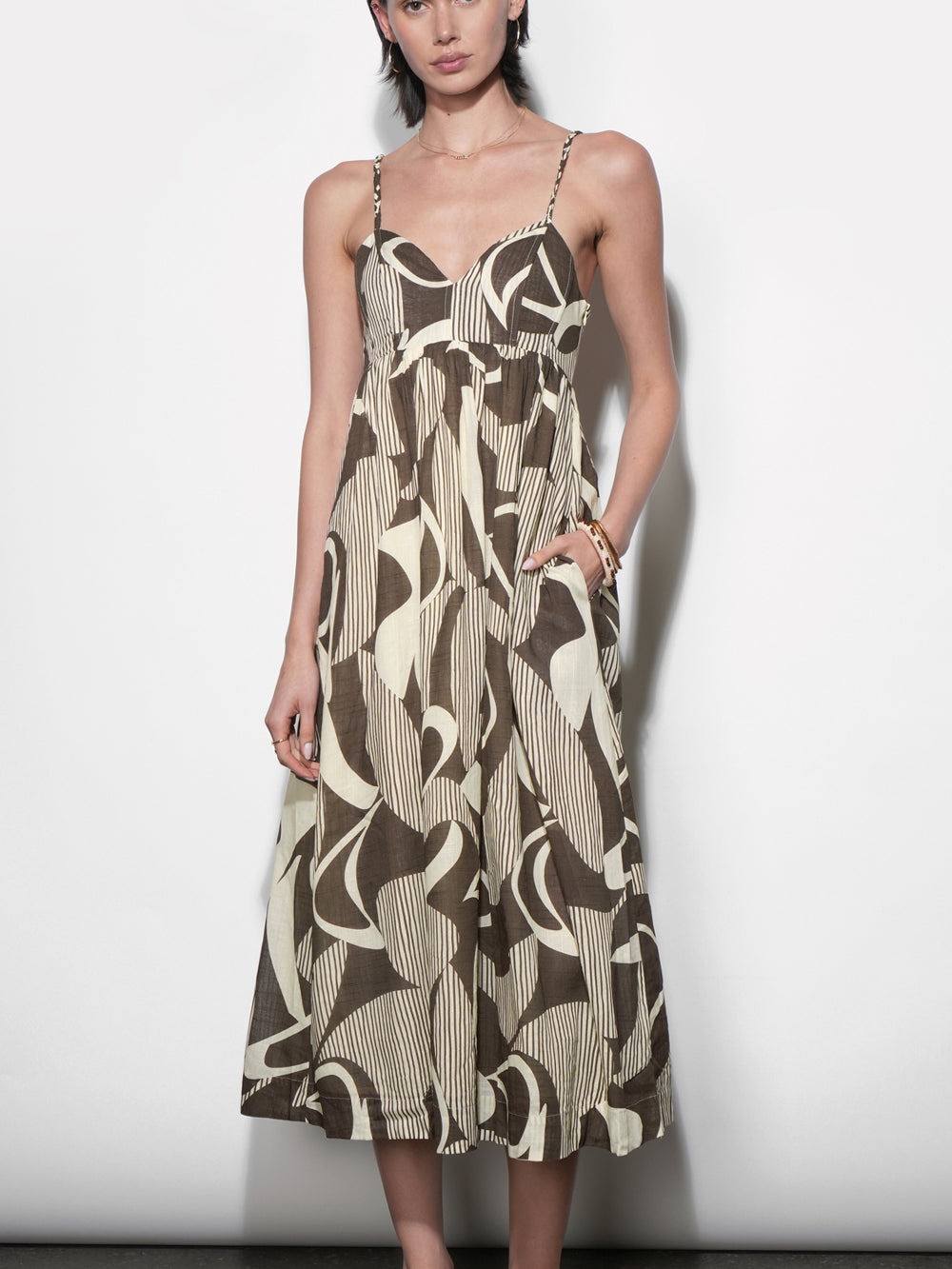 Midi dress in olive brown and cream abstract geometric print with fine stripe texture, sweetheart neckline, thin straps, empire waist, full gathered skirt, hand in side pocket