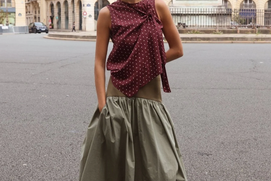 Sage green cotton maxi skirt with full gathered hem, worn with burgundy polka dot knotted top and red loafers, styled on a Paris street with equestrian statue behind.