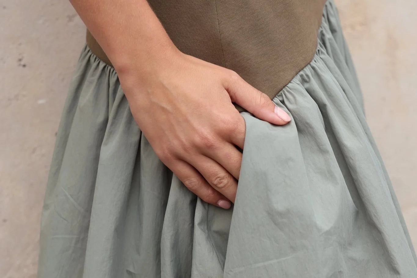 Close-up of a deep side pocket on a sage green gathered cotton skirt, hand pulling fabric open to reveal pocket depth, khaki structured waistband above.