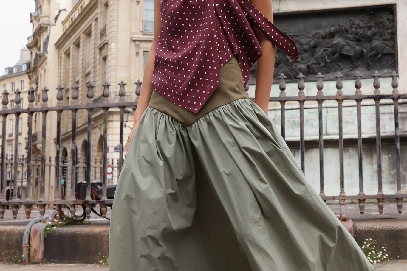 Sage green full-length gathered maxi skirt with olive fitted waistband, styled with burgundy polka dot bow top and burgundy loafers, shot outdoors in Paris near an equestrian