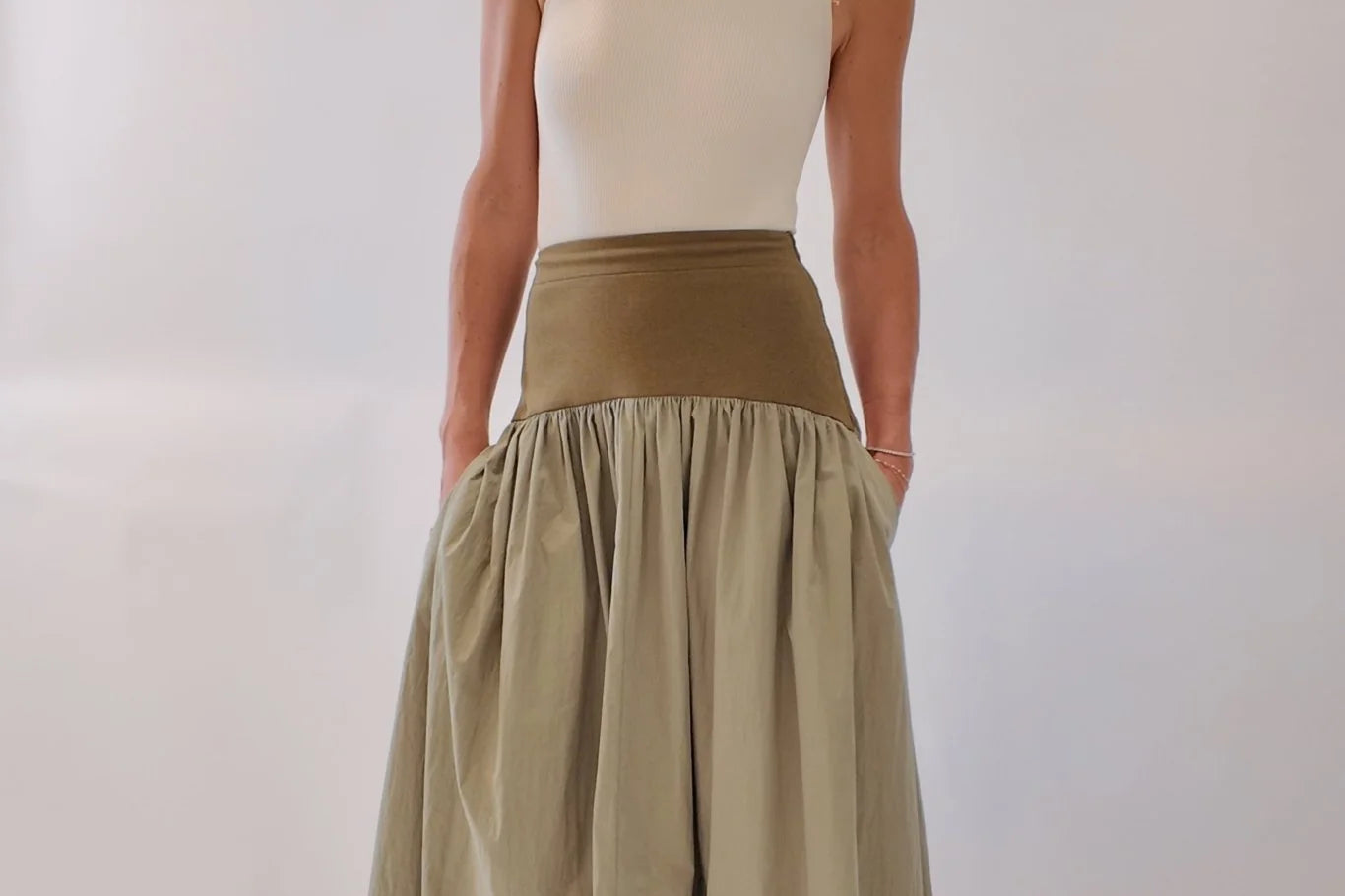 Sage green gathered maxi skirt with wide olive structured waistband, styled with cream tank and tan leather mules, front-facing full-length view showing voluminous draped