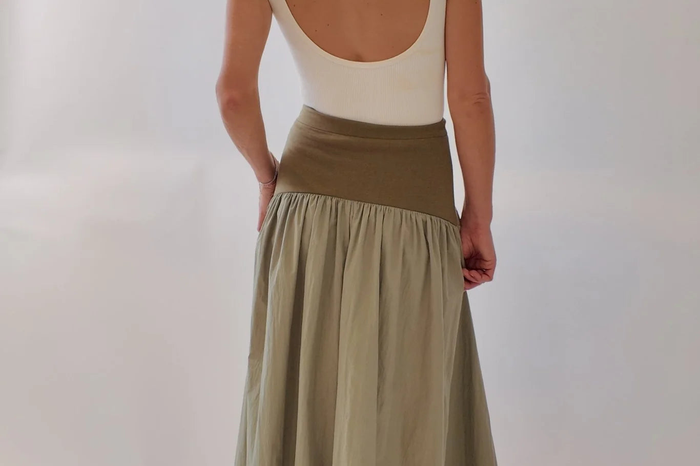 Back view of olive and sage green block maxi skirt with wide knit waistband and gathered flowing skirt, styled with a cream low-back bodysuit and tan mules.