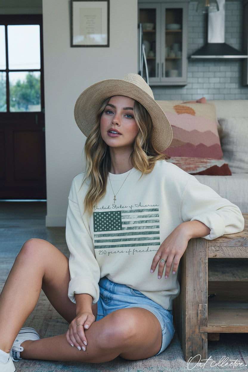 Oversized fleece crew neck with crosshatch American flag graphic, paired with denim cutoffs and straw hat