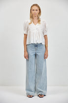 Flowy white ruffle blouse tucked loosely into wide-leg light wash jeans, full-length front view, black sandals, gold jewelry.