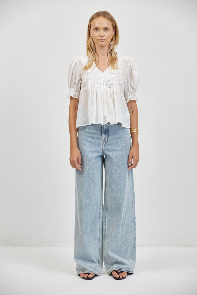 Flowy white ruffle blouse tucked loosely into wide-leg light wash jeans, full-length front view, black sandals, gold jewelry.