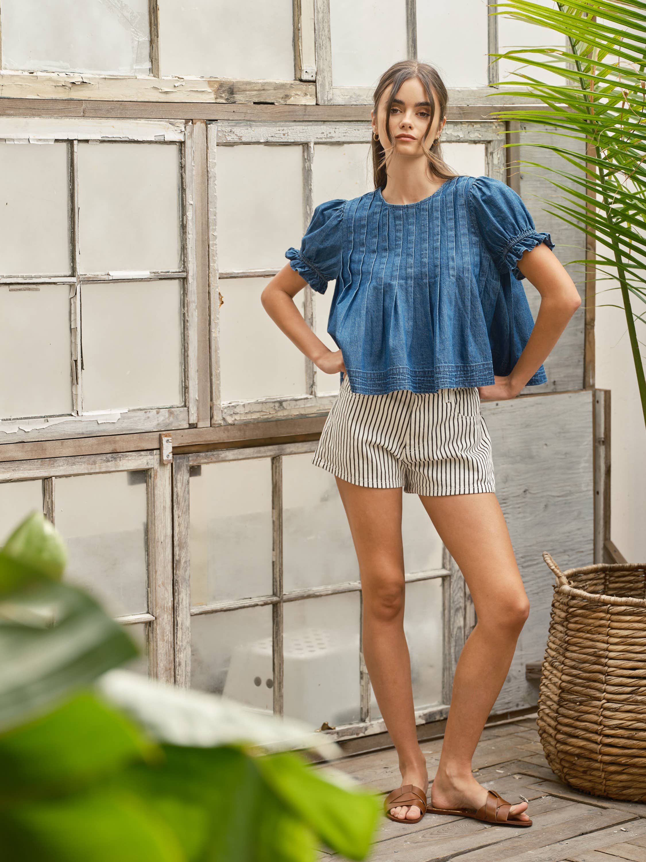 Sailor stripe cotton shorts styled with a medium-wash denim pintuck puff-sleeve top and tan woven leather sandals, full-length front view.