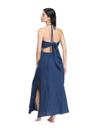 Back view of flowy navy maxi dress, open back with waist tie knot, halter cords, raw fringe hem, side slit skirt panel.