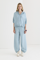 Relaxed slate blue cotton jogger trouser with gathered cuffed hem, elastic drawstring waist, worn with matching zip hoodie and white sneakers, full-length front view.