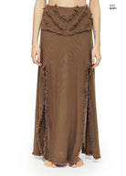 Earthy brown maxi skirt in open-weave cotton with raw fringe trim along V-shaped front yokes, side slits, and hem. Fluid A-line silhouette, low-rise fit, worn barefoot against
