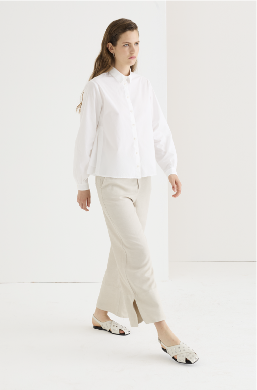 Oversized white cotton poplin shirt, boxy cropped fit, balloon sleeves with cuffed wrists, worn over sand linen wide-leg trousers with a front slit, paired with woven mule flats.