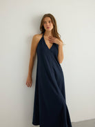 Deep navy halter maxi dress with V-neckline and subtle center front seam, A-line silhouette skimming to the floor, slub-textured natural fabric with soft matte finish.