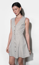 Sleeveless cream and black pinstripe mini dress with deep V-neckline, matte brass snap buttons, and angled panel skirt — fitted waist, front view, mid-thigh length.