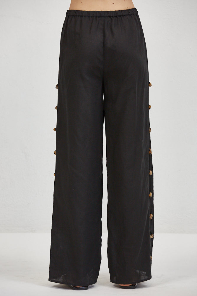 Wide-leg linen trousers, back view, elastic waist, columns of small hand-knotted fabric buttons along both