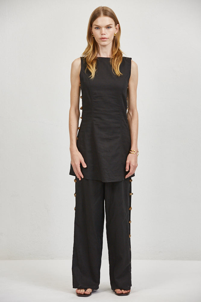 Wide-leg linen trousers with hand-knotted fabric buttons along outer seams, worn with matching sleeveless