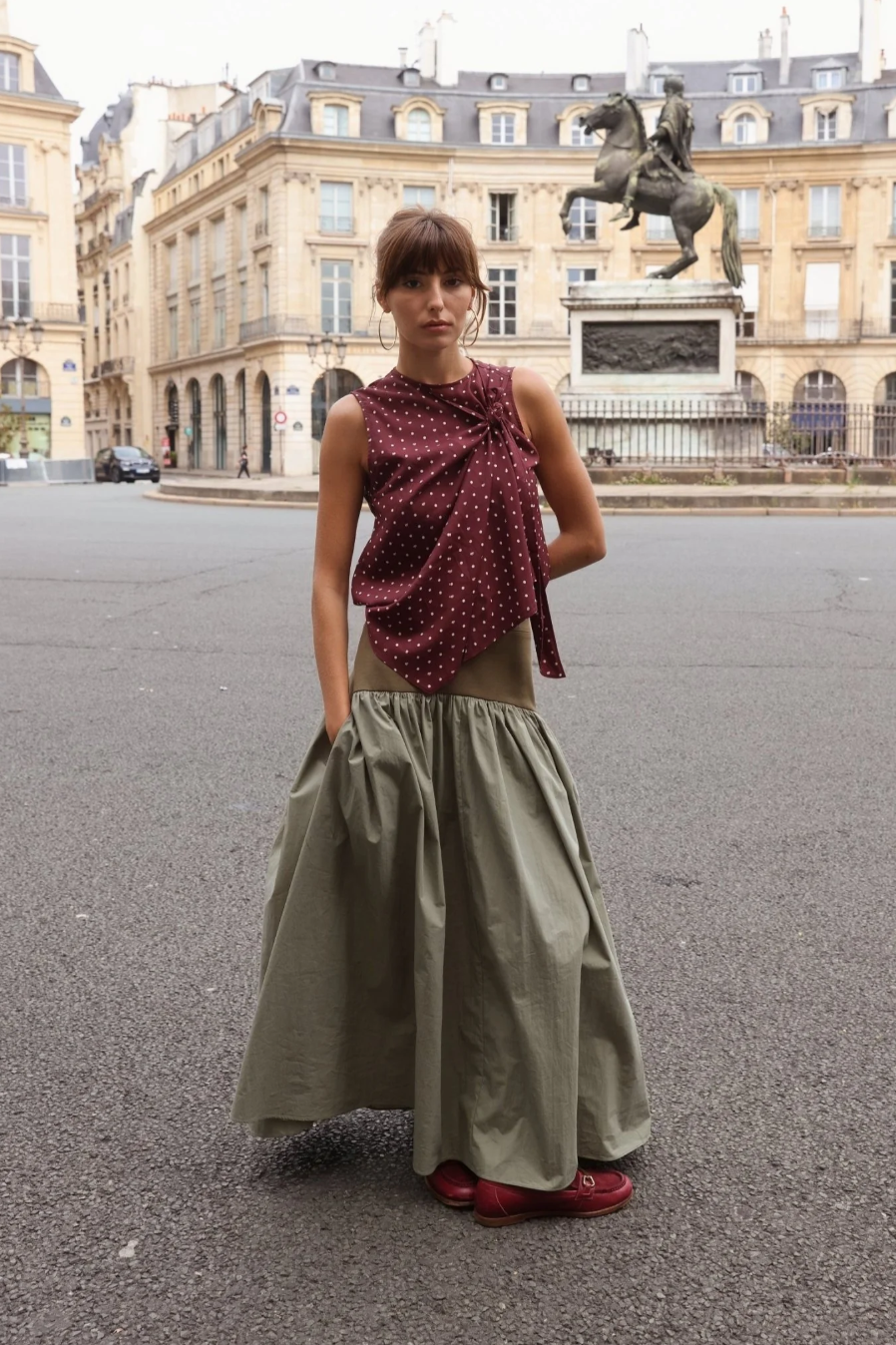 Sage green cotton maxi skirt with full gathered hem, worn with burgundy polka dot knotted top and red loafers, styled on a Paris street with equestrian statue behind.
