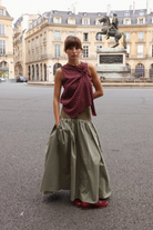 Sage green cotton maxi skirt with full gathered hem, worn with burgundy polka dot knotted top and red loafers, styled on a Paris street with equestrian statue behind.