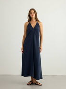 Navy halter maxi dress, deep V-neck, clean center front seam, A-line silhouette in textured slub fabric, paired with black strappy flat sandals.