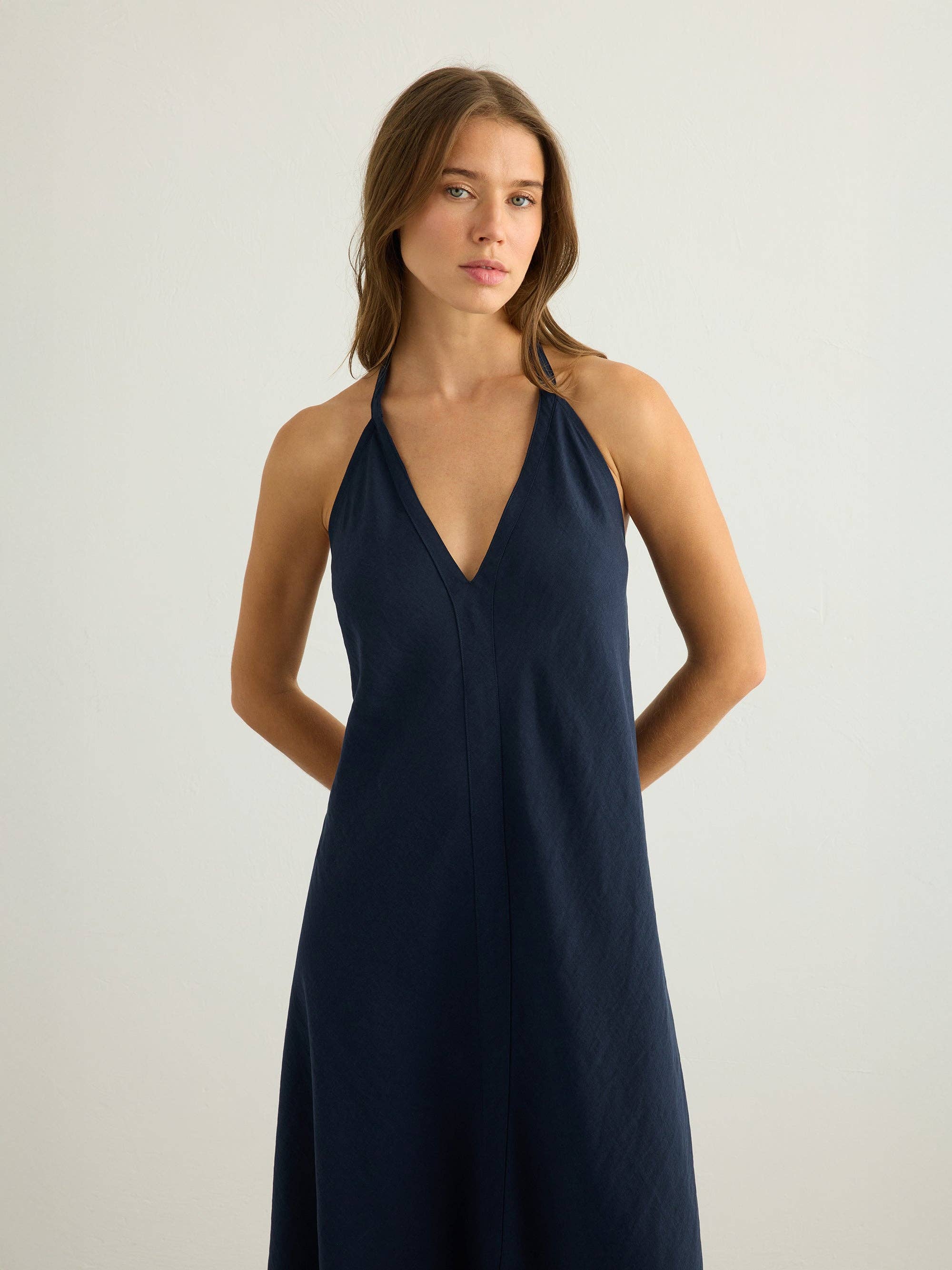 Navy halter maxi dress with deep V-neckline and clean center seam, A-line silhouette in textured slub fabric, worn against a white background, cropped at mid-thigh