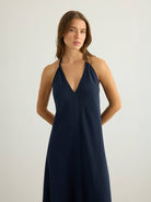 Navy halter maxi dress with deep V-neckline and clean center seam, A-line silhouette in textured slub fabric, worn against a white background, cropped at mid-thigh