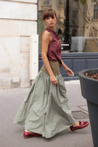 Sage green full-length maxi skirt with olive block waistband, deeply gathered lightweight skirt panel, styled with burgundy polka dot top and burgundy loafers, street setting