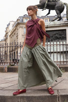 Sage green full-length gathered maxi skirt with olive fitted waistband, styled with burgundy polka dot bow top and burgundy loafers, shot outdoors in Paris near an equestrian