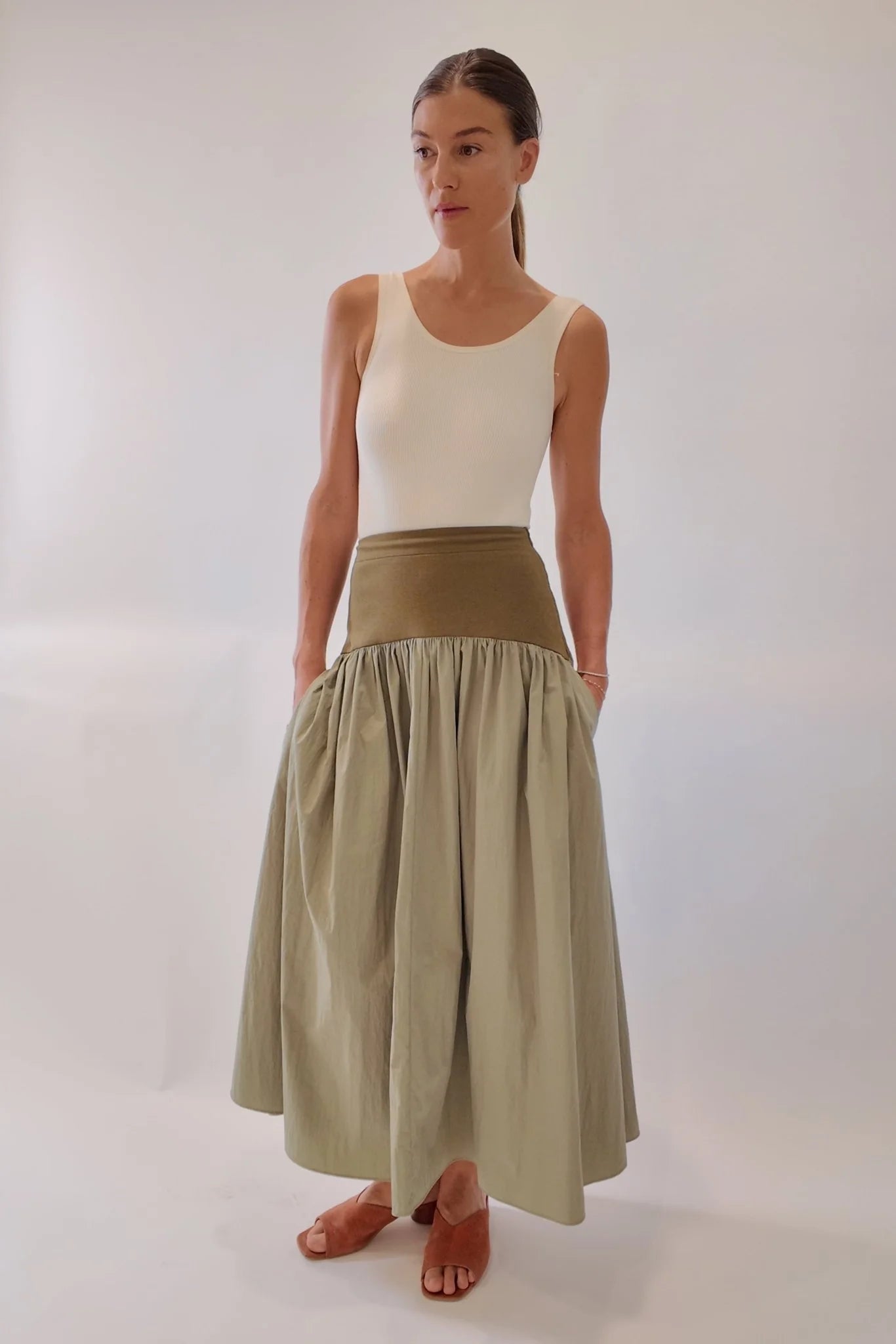 Sage green gathered maxi skirt with wide olive structured waistband, styled with cream tank and tan leather mules, front-facing full-length view showing voluminous draped