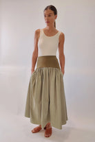 Sage green gathered maxi skirt with wide olive structured waistband, styled with cream tank and tan leather mules, front-facing full-length view showing voluminous draped