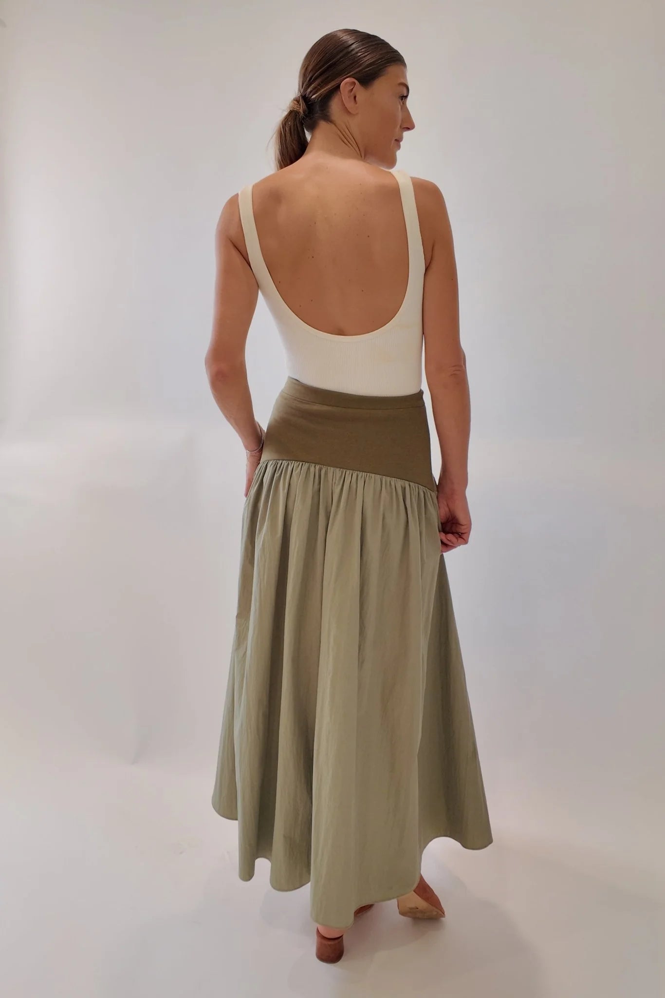 Back view of olive and sage green block maxi skirt with wide knit waistband and gathered flowing skirt, styled with a cream low-back bodysuit and tan mules.